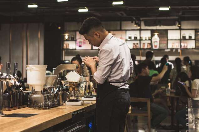 men's brown dress shirt and black pants making cofee inside a cafe
